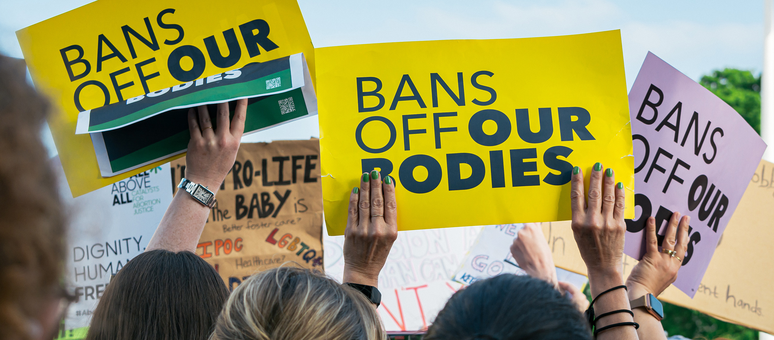 protestors hold signs that say "bans off our bodies"