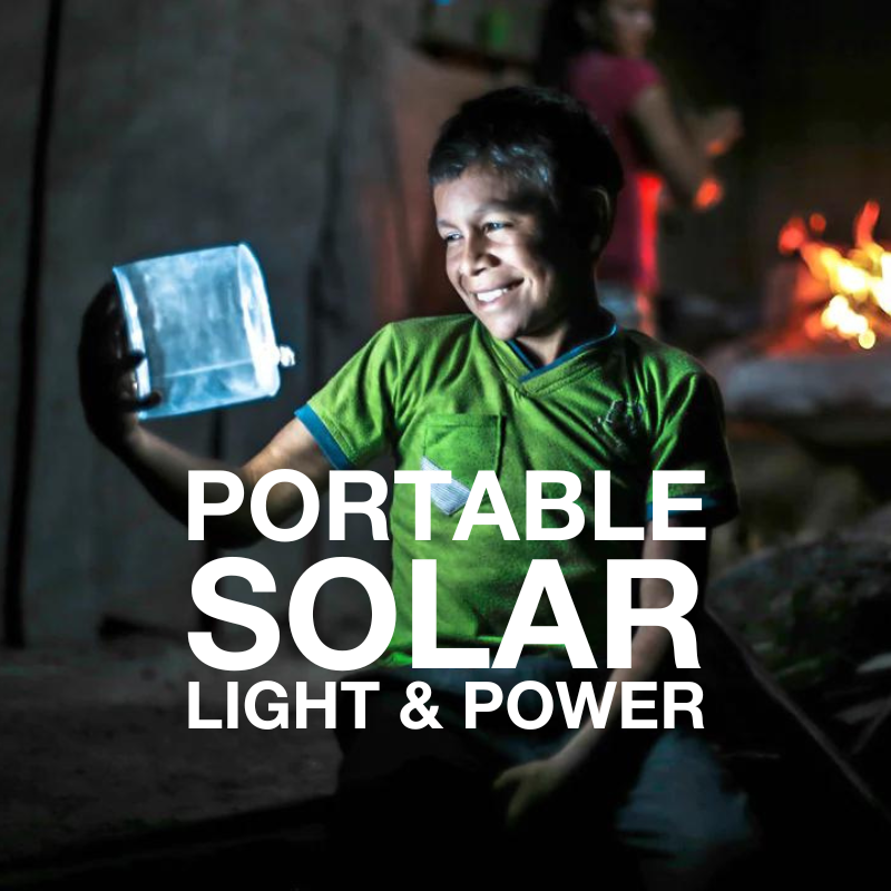 photograph of a young boy holding a portable solar light in the evening with his face lit and fire in the background